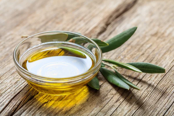 Aceite de oliva y ramita de oliva sobre una mesa de madera — Foto de Stock