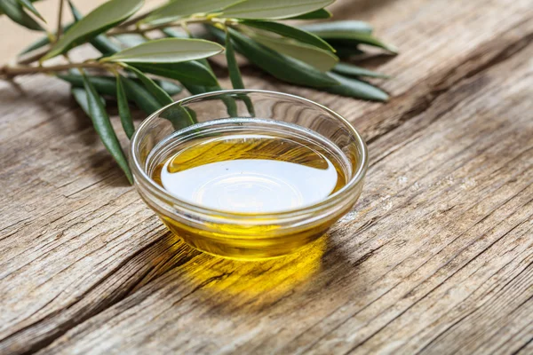 Aceite de oliva y ramita de oliva sobre una mesa de madera — Foto de Stock