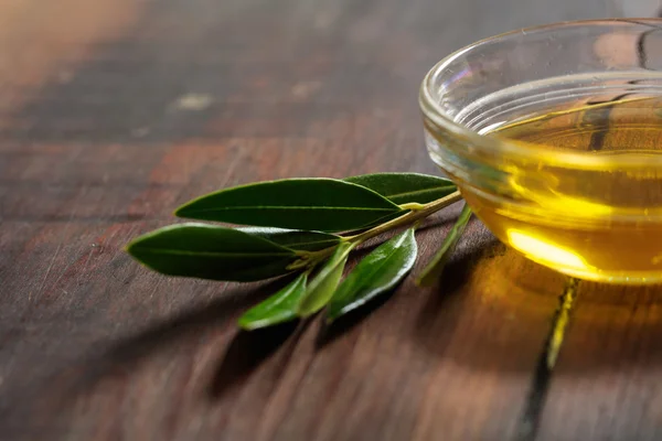 Оливковое масло и оливковая веточка на деревянном столе — стоковое фото
