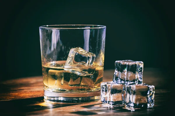 Glas whiskey en ijsblokjes op houten teller — Stockfoto