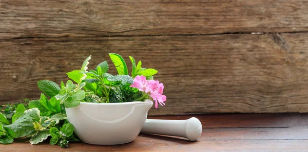 Herbs in a mortar on wooden background — Stock Photo, Image