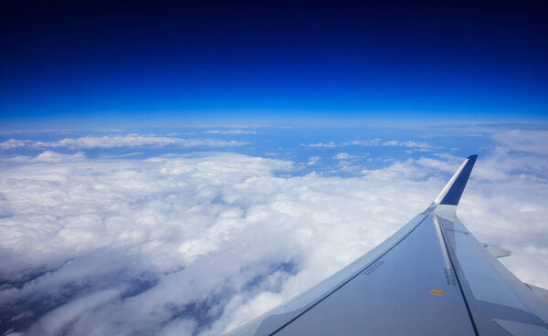 Plane wing over clouds on a blue sky background