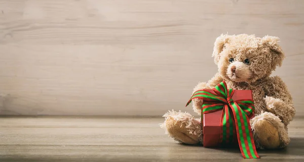 Teddy bear holdimg a gift on a wooden floor — Stock Photo, Image