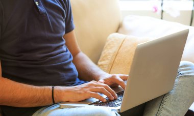 Adam evde kanepede oturan bir dizüstü bilgisayar ile çalışma