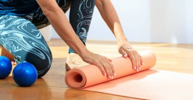 Kadın bir yoga mat ahşap zemin üzerinde haddeleme