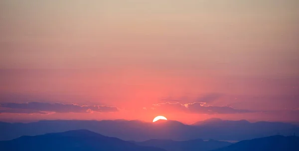 Wunderschöner Sonnenuntergang am Himmel über Bergen im Hintergrund. die Sonne steht in der Mitte. — Stockfoto