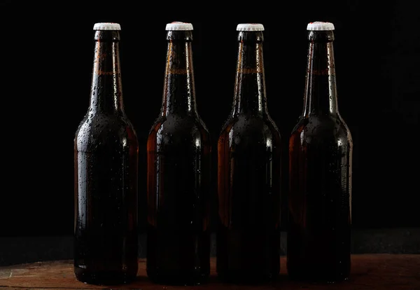 Primer plano de cuatro botellas de cerveza aisladas sobre fondo negro —  Fotos de Stock