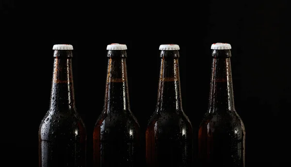 Primer plano de cuatro botellas de cerveza aisladas sobre fondo negro —  Fotos de Stock