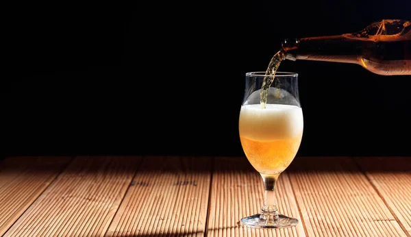 Versare la birra in un bicchiere su un tavolo di legno, sfondo scuro — Foto Stock