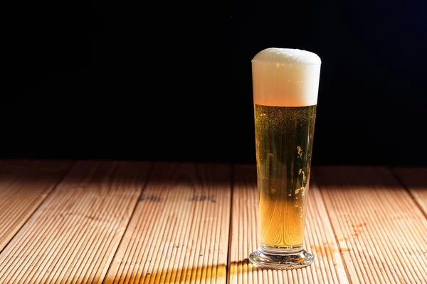 Un bicchiere di birra su un tavolo di legno, sfondo scuro — Foto Stock