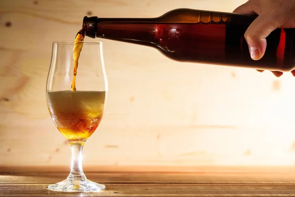 Наливание пива в стакан на деревянный стол — стоковое фото