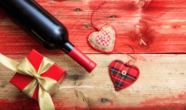 Sevgililer günü. Kırmızı şarap şişesi, hediye ve kalpler kırmızı ahşap zemin üzerinde