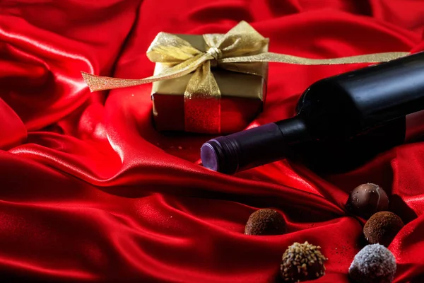 Saint Valentin. Bouteille de vin rouge, chocolats et un cadeau sur satin rouge — Photo