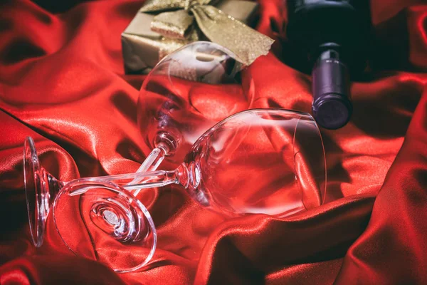 San Valentino. Bottiglia di vino rosso, bicchieri e un regalo su raso rosso — Foto Stock