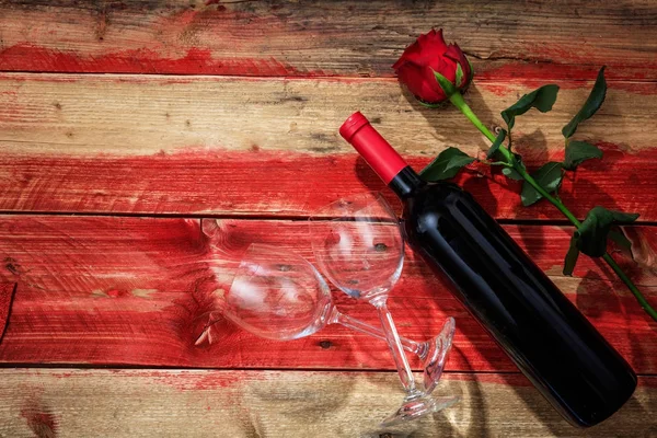 Día de San Valentín. Botella de vino tinto, copas y una rosa sobre fondo de madera roja —  Fotos de Stock