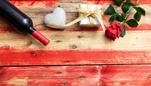 Dia dos Namorados. Garrafa de vinho tinto, rosa e um presente no fundo de madeira — Fotografia de Stock