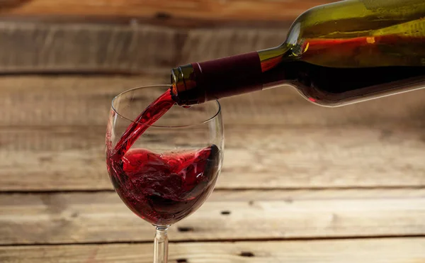 Vörös bor ömlött egy üveg, fa háttér — Stock Fotó