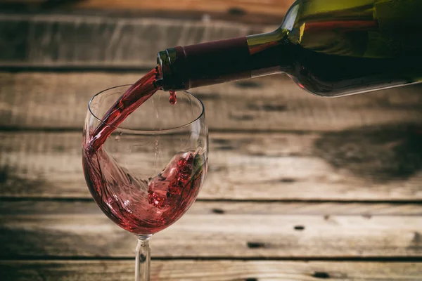 Despejar vinho tinto em um copo no fundo de madeira — Fotografia de Stock
