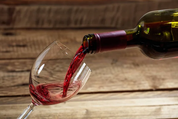 Наливание красного вина в стакан на деревянном фоне — стоковое фото
