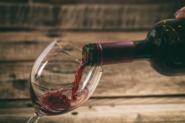 Verser du vin rouge dans un verre sur fond de bois — Photo