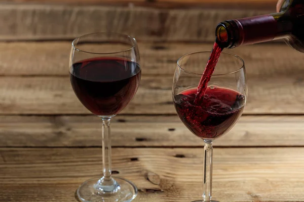 Versare il vino rosso in un bicchiere su fondo di legno — Foto Stock