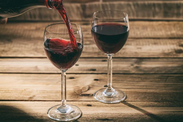 Versare il vino rosso in un bicchiere su fondo di legno — Foto Stock