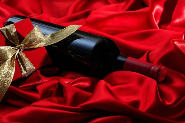 Ημέρα του Αγίου Βαλεντίνου. Κόκκινο μπουκάλι κρασί και ένα δώρο στο κόκκινο σατέν — Φωτογραφία Αρχείου