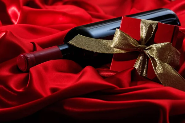 Saint Valentin. Bouteille de vin rouge et cadeau sur satin rouge — Photo