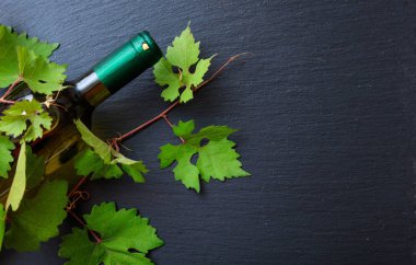 Beyaz şarap şişesi ve taze üzüm yaprakları siyah arka plan üzerine, kopya alanı