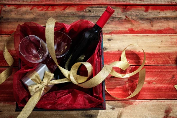 San Valentino. Bottiglia di vino rosso, bicchieri e un regalo in una scatola, sfondo in legno con copyspace — Foto Stock