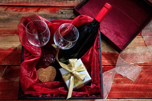 Saint Valentin. Bouteille de vin rouge, verres et un cadeau dans une boîte, fond en bois — Photo