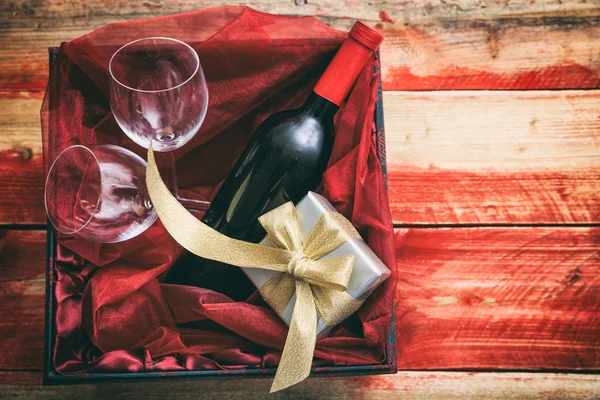 San Valentino. Bottiglia di vino rosso, bicchieri e un regalo in una scatola, sfondo in legno con copyspace — Foto Stock