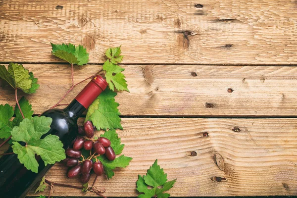 Garrafa de vinho tinto e uvas frescas em fundo de madeira, espaço de cópia — Fotografia de Stock