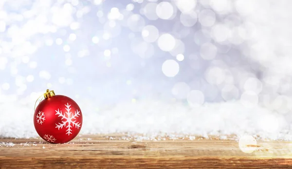 Bola de Natal em uma mesa de madeira, fundo bokeh nevado — Fotografia de Stock