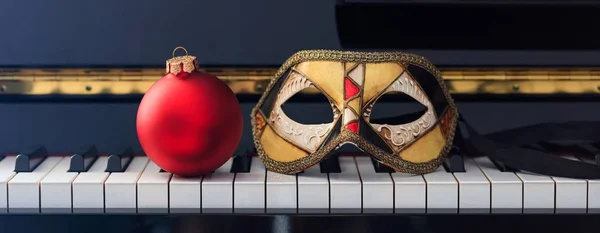 Palla rossa di Natale e maschera di carnevale sulla tastiera del pianoforte, vista frontale — Foto Stock