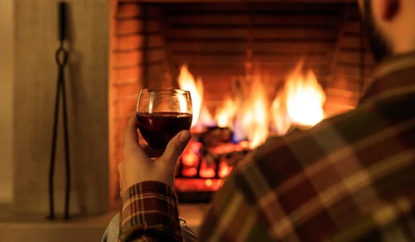 Человек держит бокал красного вина на горящем фоне камина — стоковое фото