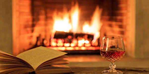 Verre de brandy et un livre sur fond de cheminée en feu — Photo