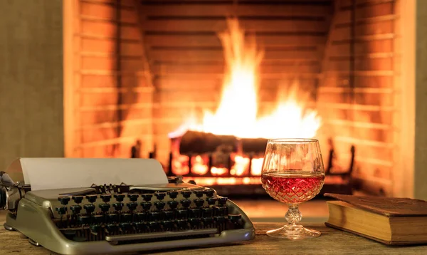 Verre de brandy et une machine à écrire sur fond de cheminée en feu — Photo