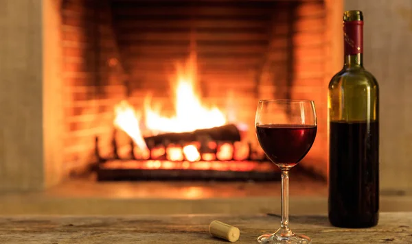 A glass and a bottle of red wine on burning fireplace background — Stock Photo, Image