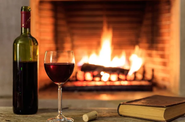 Red wine and a book on burning fireplace background — Stock Photo, Image