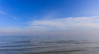 Sakin deniz ve mavi gökyüzü beyaz bulutlar arka plan ile. Bir uçak sinek ufukta.