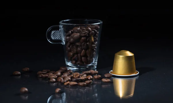 Капсула эспрессо, чашка кофе и бобы на черном фоне, вид крупным планом с деталями — стоковое фото