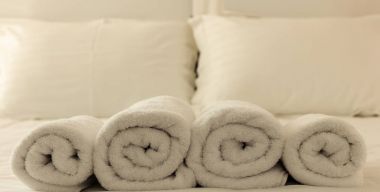 Otel yatak odası. Beyaz kabarık, yatağa satır, keten çarşaflar ve yastıklar havlu haddelenmiş. Portre.