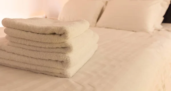 Hotel bedroom. White fluffy, folded towels, linen sheets and pillows on bed. Close up view. — Stock Photo, Image
