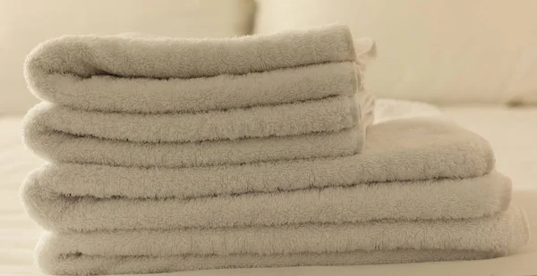Hotel bedroom. White fluffy, folded towels, linen sheets and pillows on bed. Close up view.