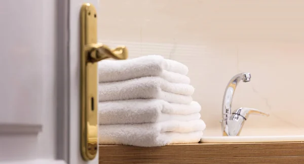 Μπάνιο του ξενοδοχείου από την ανοικτή πόρτα. Λευκά σεντόνια διπλωμένα δίπλα στο νεροχύτη. Κοντινό πλάνο, θαμπάδα σκηνικό. — Φωτογραφία Αρχείου