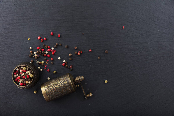 Peppercorns and a bronze pepper mill on black background, top view, copy space