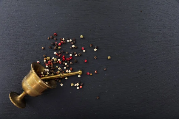 Peppercorns y un mortero de bronce sobre fondo negro, vista superior, espacio para copiar — Foto de Stock