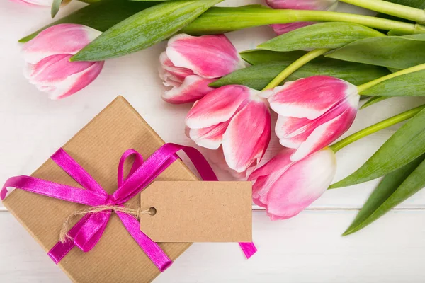 Día de las madres. Tulipanes rosados y un regalo de tarjeta en blanco sobre fondo blanco, vista superior, espacio para copiar — Foto de Stock