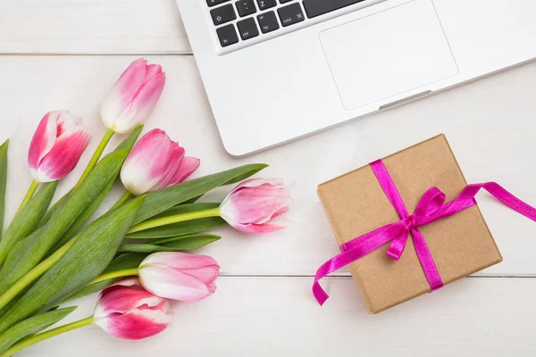 Dia das mulheres. Tulipas cor-de-rosa, laptop e um presente em uma mesa branca, vista superior — Fotografia de Stock